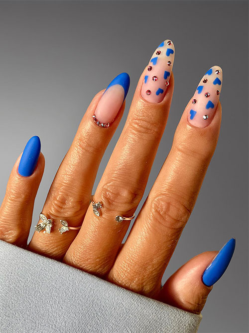 Matte blue Valentine's Day nails with a French tip nail adorned with silver rhinestones and two accent nude nails with hearts