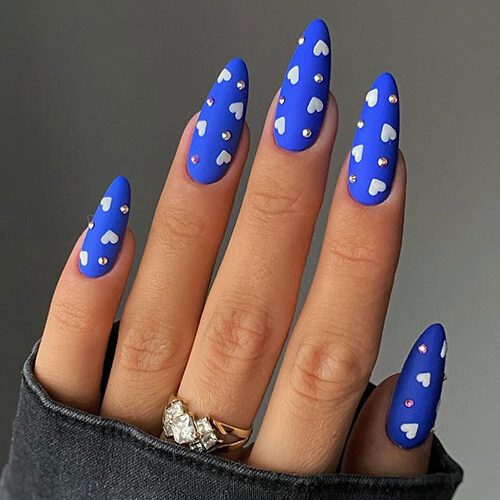 Matte cobalt blue Valentine's Day nails adorned with white heart shapes and rhinestones