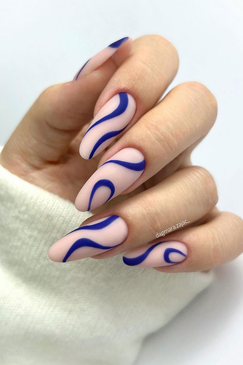 Matte long almond-shaped nude nails adorned with navy blue swirl nail art