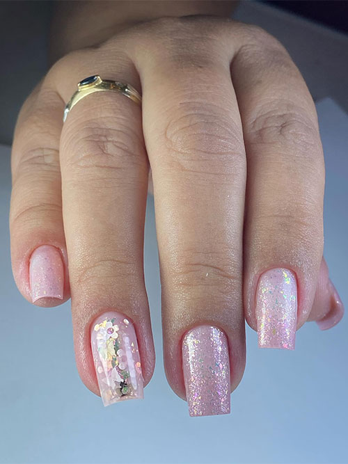 Shimmering nude nails adorned with tiny flowers and glitter on an accent nail Shimmering nude nails adorned with tiny flowers and glitter on an accent nail