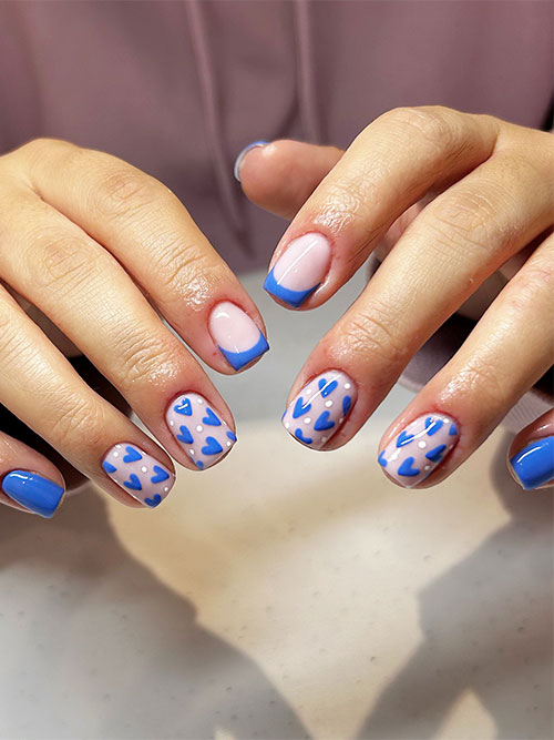 Short blue nails with an accent French tip nail and another two nude nails adorned with white dots and tiny blue heart shapes