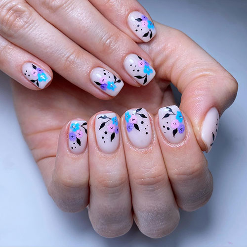 Short flower spring nails over nude base color and feature pastel flowers in blue, pink, and purple nail colors with black leaves Short flower spring nails over nude base color and feature pastel flowers in blue, pink, and purple nail colors with black leaves