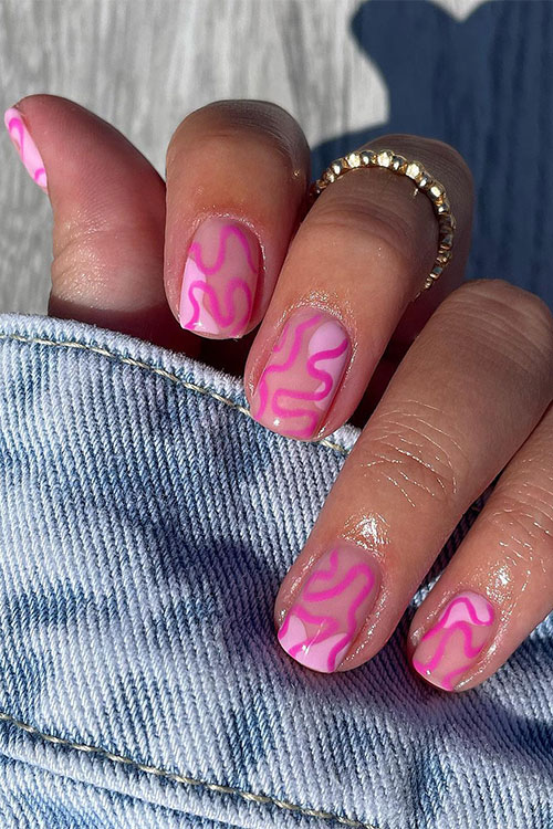 Short negative space light pink nails over nude base color and adorned with hot pink swirls