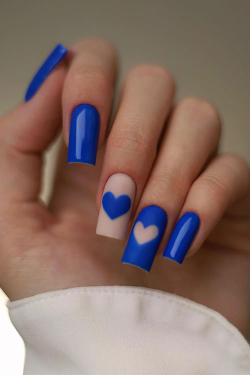 Square-shaped glossy blue nails with a matte nude accent nail adorned with a blue heart shape