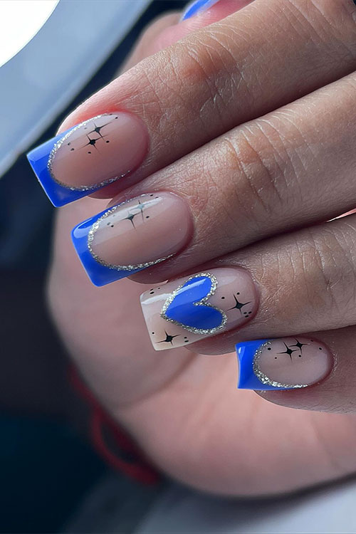 Square-shaped gold glitter and blue double French tip nails adorned with tiny black stars and a nude accent with a blue heart
