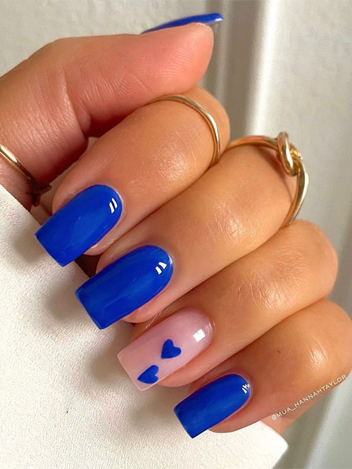 Square-shaped royal blue Valentine's Day nails with an accent nude nail adorned with two royal blue heart shapes