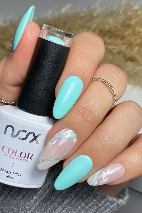 Fancy mint green spring nails with two nude accent nails adorned with white leaves, silver glitter swirls, and mint swirls Fancy mint green spring nails with two nude accent nails adorned with white leaves, silver glitter swirls, and mint swirls