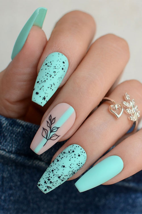 Matte coffin mint green nails with two accent nails adorned with black speckles and a nude accent with a black leaf