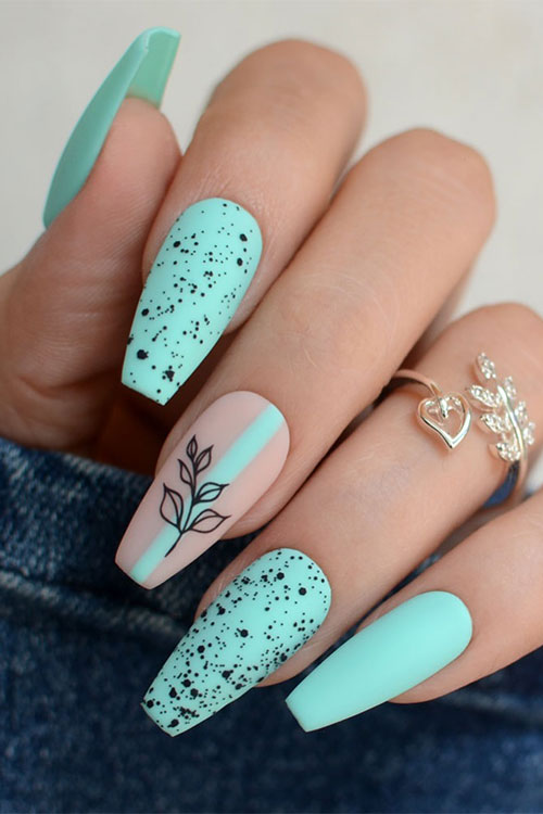 Matte coffin mint green nails with two accent nails adorned with black speckles and a nude accent with a black leaf Matte coffin mint green nails with two accent nails adorned with black speckles and a nude accent with a black leaf