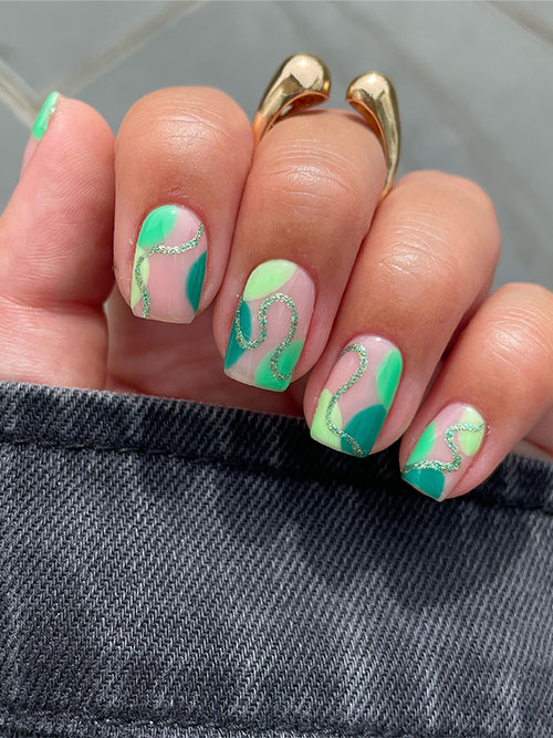 Short abstract march nails take on a playful twist adorned in various shades of green and glitter swirls!