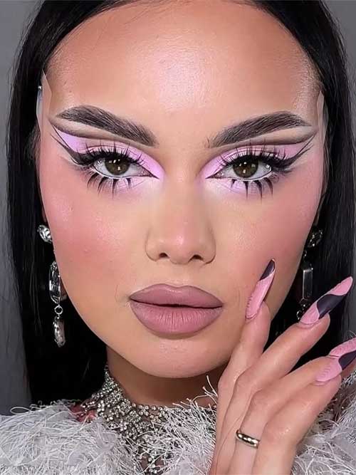 Bold graphic makeup with pink eyeshadow, black winged liner, white accents, and individual lower lashes for a striking look. Bold graphic makeup with pink eyeshadow, black winged liner, white accents, and individual lower lashes for a striking look.