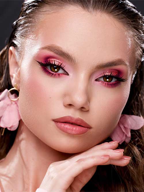 Bold pink and red eye makeup with winged liner, soft pink lips, floral earrings, and sleek hairstyle for a glamorous look. Bold pink and red eye makeup with winged liner, soft pink lips, floral earrings, and sleek hairstyle for a glamorous look.