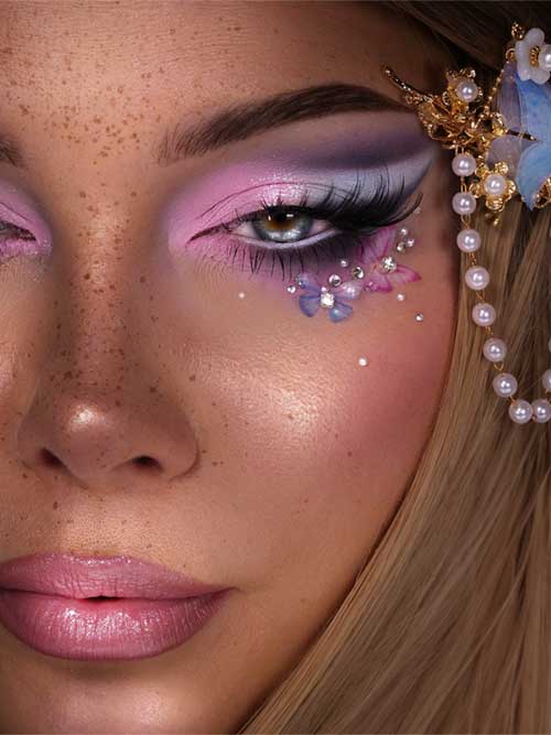 Fairy-inspired makeup features pink, lavender, and grey eyeshadow, adorned with flowers and rhinestones, plus glossy pink lips. Fairy-inspired makeup features pink, lavender, and grey eyeshadow, adorned with flowers and rhinestones, plus glossy pink lips.