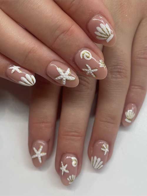 Seashell nail design with white seashells and starfish on a nude base, accented with shimmering gold glitter for a beachy vibe. Seashell nail design with white seashells and starfish on a nude base, accented with shimmering gold glitter for a beachy vibe.