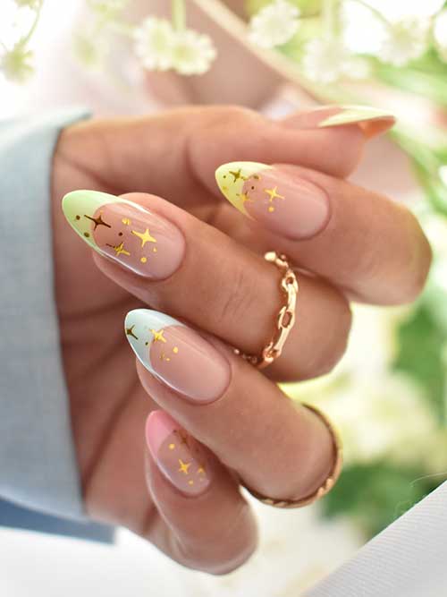 French manicure with pastel tips in pink, blue, green, and yellow, adorned with gold stars and dots on a nude base. French manicure with pastel tips in pink, blue, green, and yellow, adorned with gold stars and dots on a nude base.