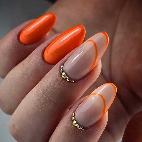 Glossy orange nails with negative space accents and gold rhinestones, blending bold color with chic elegance for any occasion.