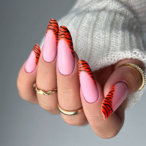 Fierce light pink nails adorned with orange and black tiger stripe French tips, ideal for making a statement at events.