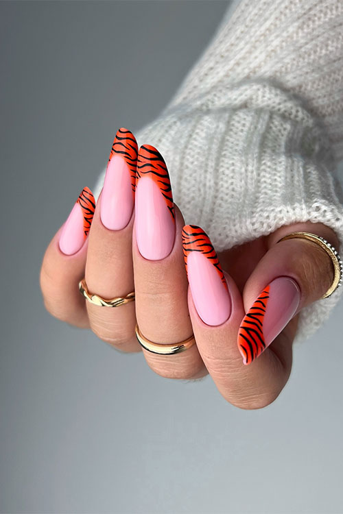 Fierce light pink nails adorned with orange and black tiger stripe French tips, ideal for making a statement at events.