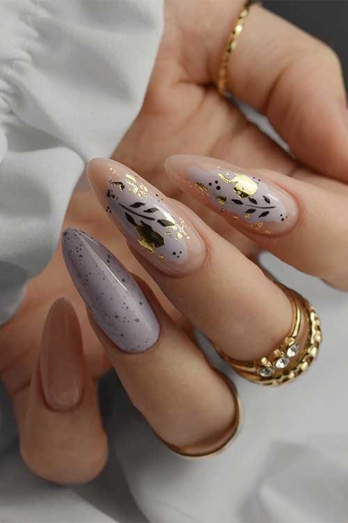 Nude almond nails with black floral designs, gold leaf accents, and one lavender-speckled nail for a bold, artistic look. Nude almond nails with black floral designs, gold leaf accents, and one lavender-speckled nail for a bold, artistic look.