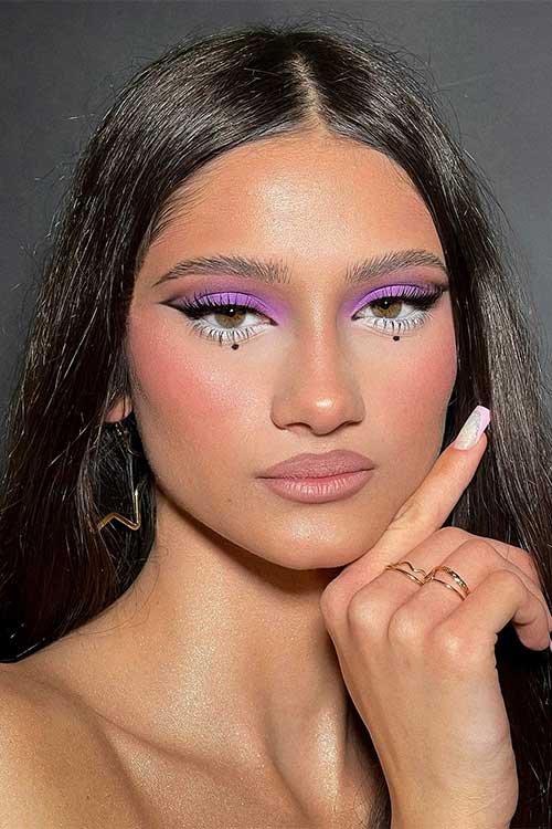Soft purple eyeshadow with a sharp black wing, whimsical white lower liner, blush, and nude lips for a chic, playful look. Soft purple eyeshadow with a sharp black wing, whimsical white lower liner, blush, and nude lips for a chic, playful look.