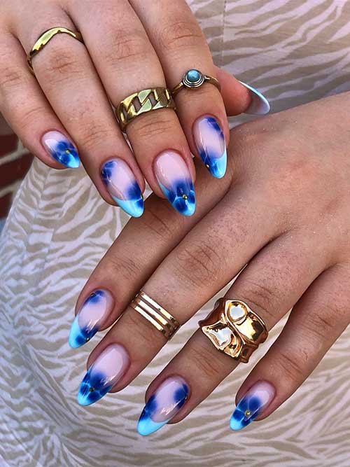 Light blue French tip nails with nude pink base, navy flowers, and gold studs, embodying summer elegance and charm.