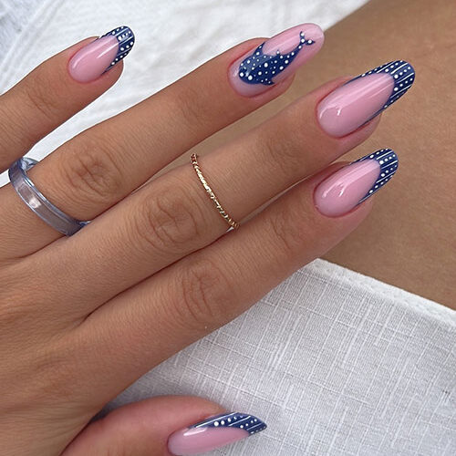 French summer nails with almond shape, blush-pink base, navy tips, playful polka dots, and a cute whale on one nail.