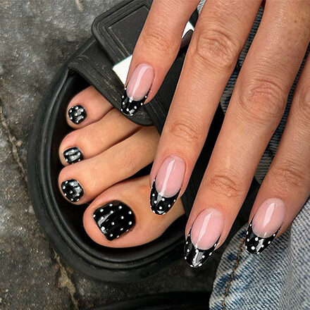 Polka dot manicure and pedicure set featuring nude nails, black tips, and white dots for a playful, chic look.