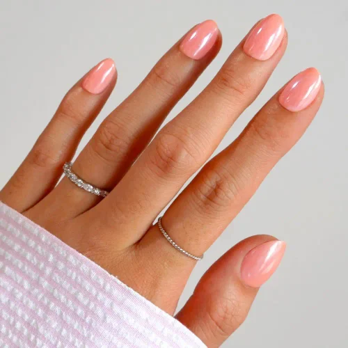 Hand featuring glossy glazed short oval peach nails with delicate rings Hand featuring glossy glazed short oval peach nails with delicate rings