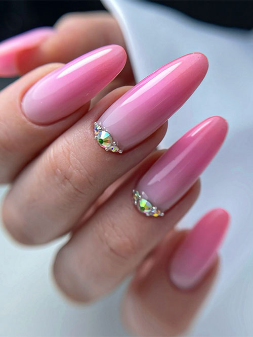 Elegant pink ombre nails transition from soft pink to bubblegum, adorned with iridescent rhinestones for added sparkle.