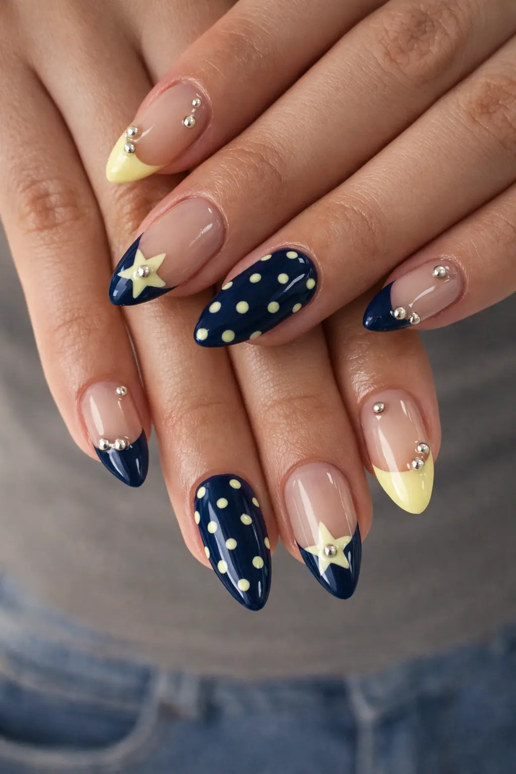 Medium almond-shaped press-on nails featuring navy blue and pale yellow designs with polka dots, star motifs, and silver bead accents.