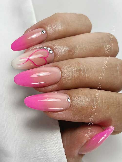 Pink ombre nails with a heart outline and rhinestones, blending elegance and romance, are stylish pink ombre nail ideas.