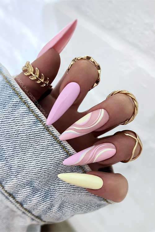 Long, pointed nails in pink, yellow, and swirls, adorned with gold rings, paired with a denim jacket for a chic look. Long, pointed nails in pink, yellow, and swirls, adorned with gold rings, paired with a denim jacket for a chic look.