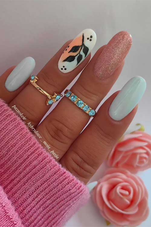 Pastel blue nails with pink glitter, abstract art on the middle finger, pink sweater, and vibrant pink roses in the background. Pastel blue nails with pink glitter, abstract art on the middle finger, pink sweater, and vibrant pink roses in the background.