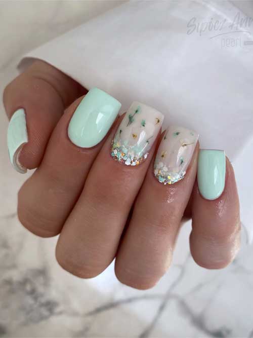 Pastel spring nails with mint green on three fingers and nude floral designs on two, accented with glittery tips. Pastel spring nails with mint green on three fingers and nude floral designs on two, accented with glittery tips.